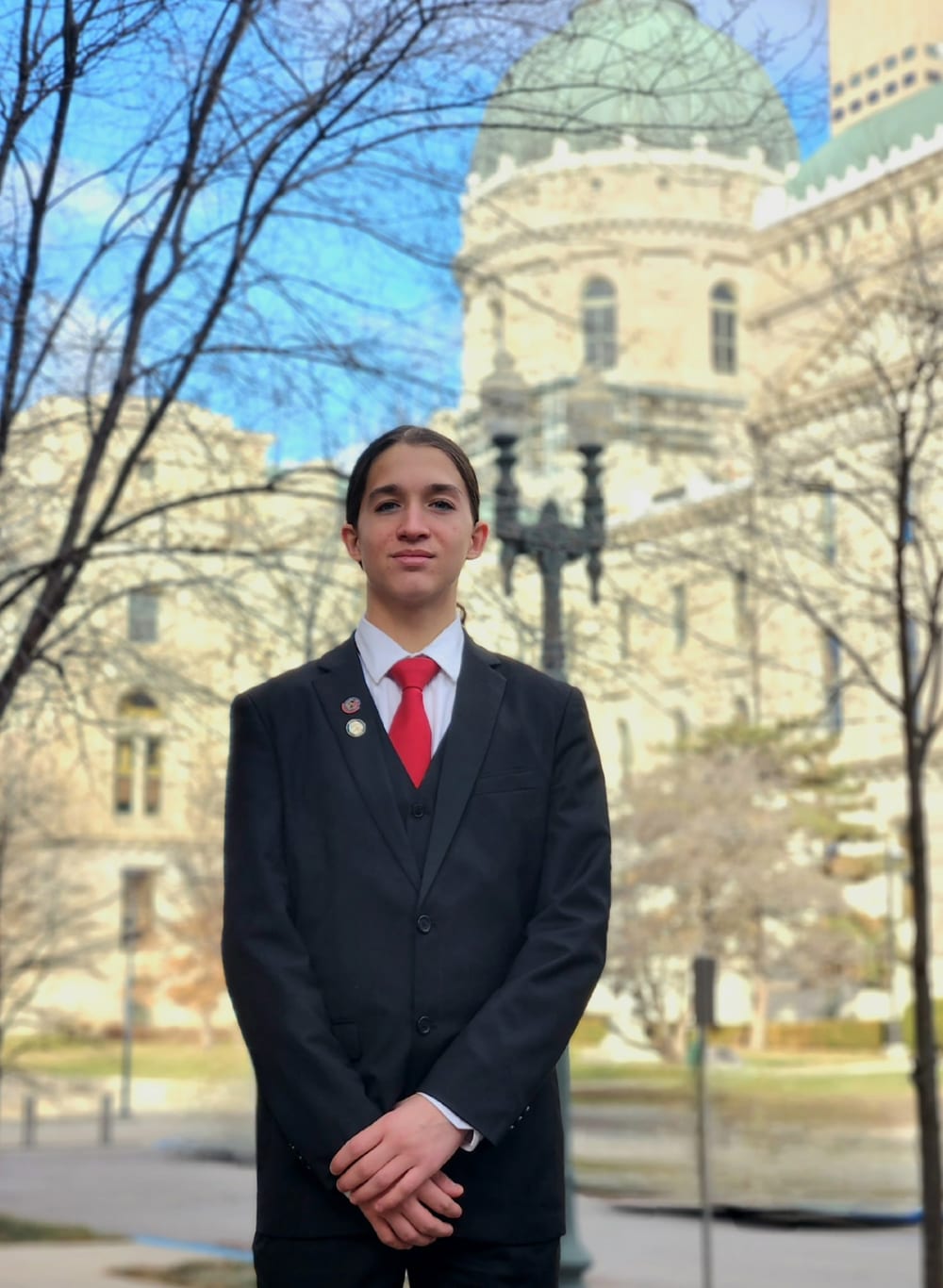 Jude Troxell, standing outside the Indiana Statehouse in a dark suit and red tie